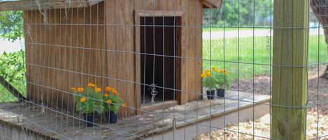 A wooden birdhouse with a wire fence, surrounded by potted plants and flowers.