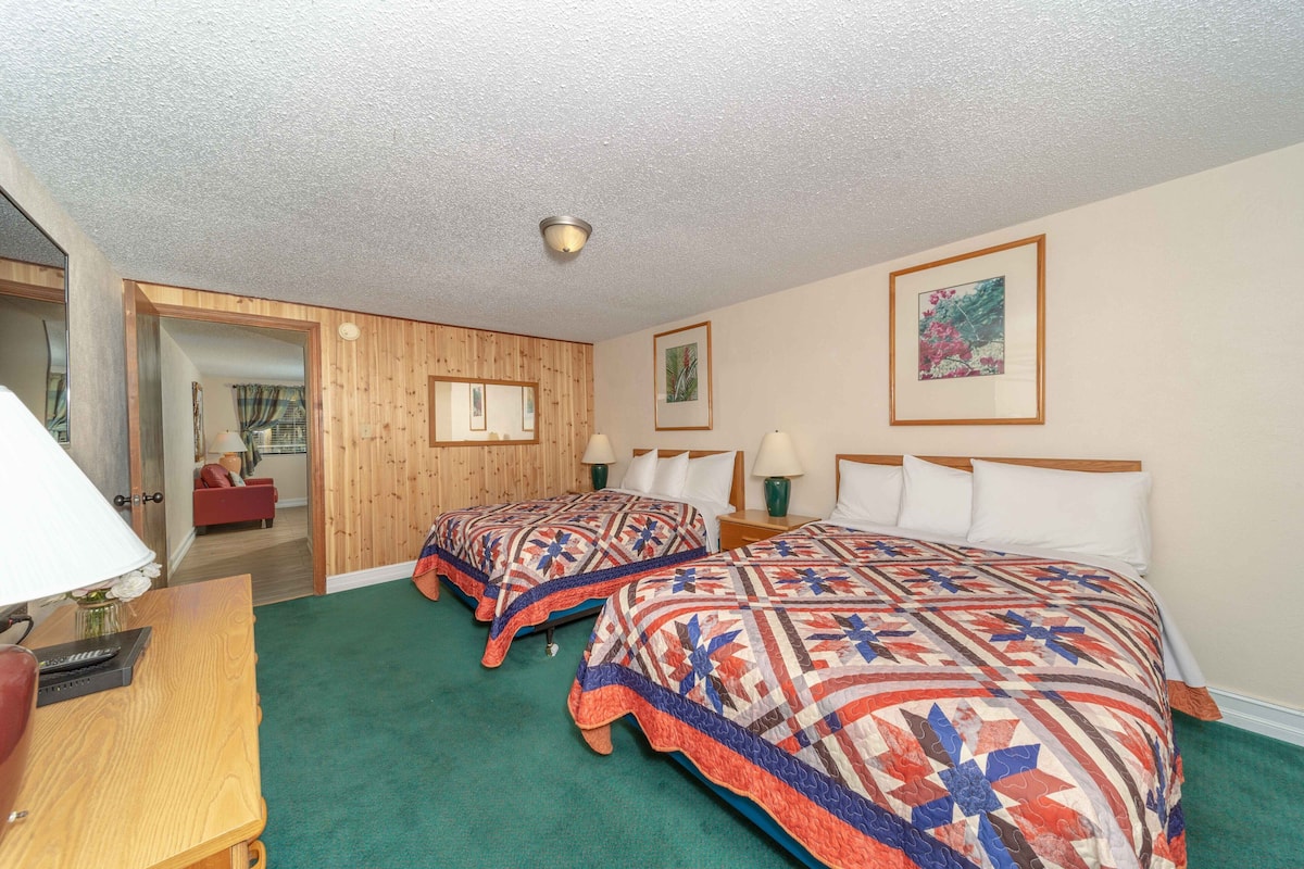 Habitación de hotel con dos camas, una pared de madera, una alfombra verde y un cuadro en la pared.
