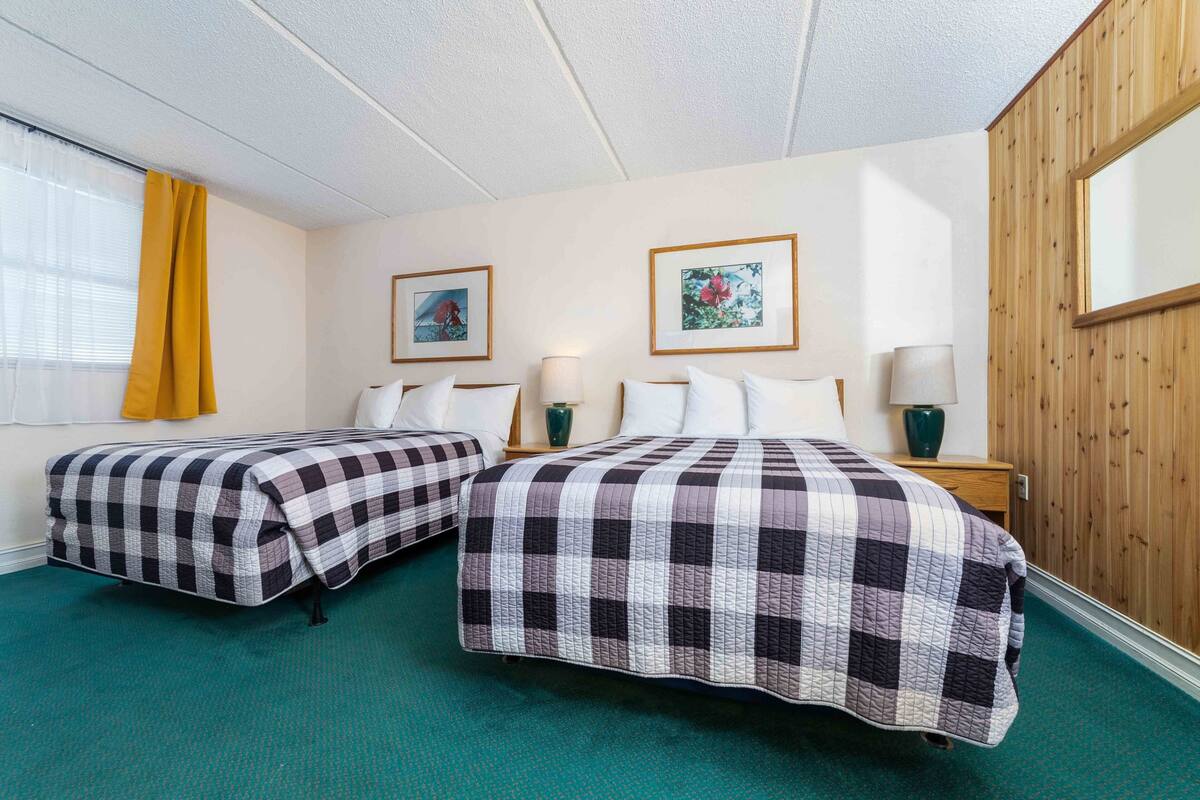Habitación de hotel con dos camas, cada una con colcha a cuadros, pared de paneles de madera y cuadros enmarcados.