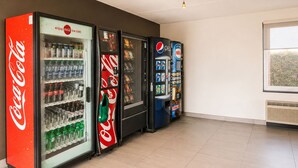 Une rangée de distributeurs automatiques aux couleurs de Coca-Cola et de Pepsi, et une fenêtre donnant sur la verdure.