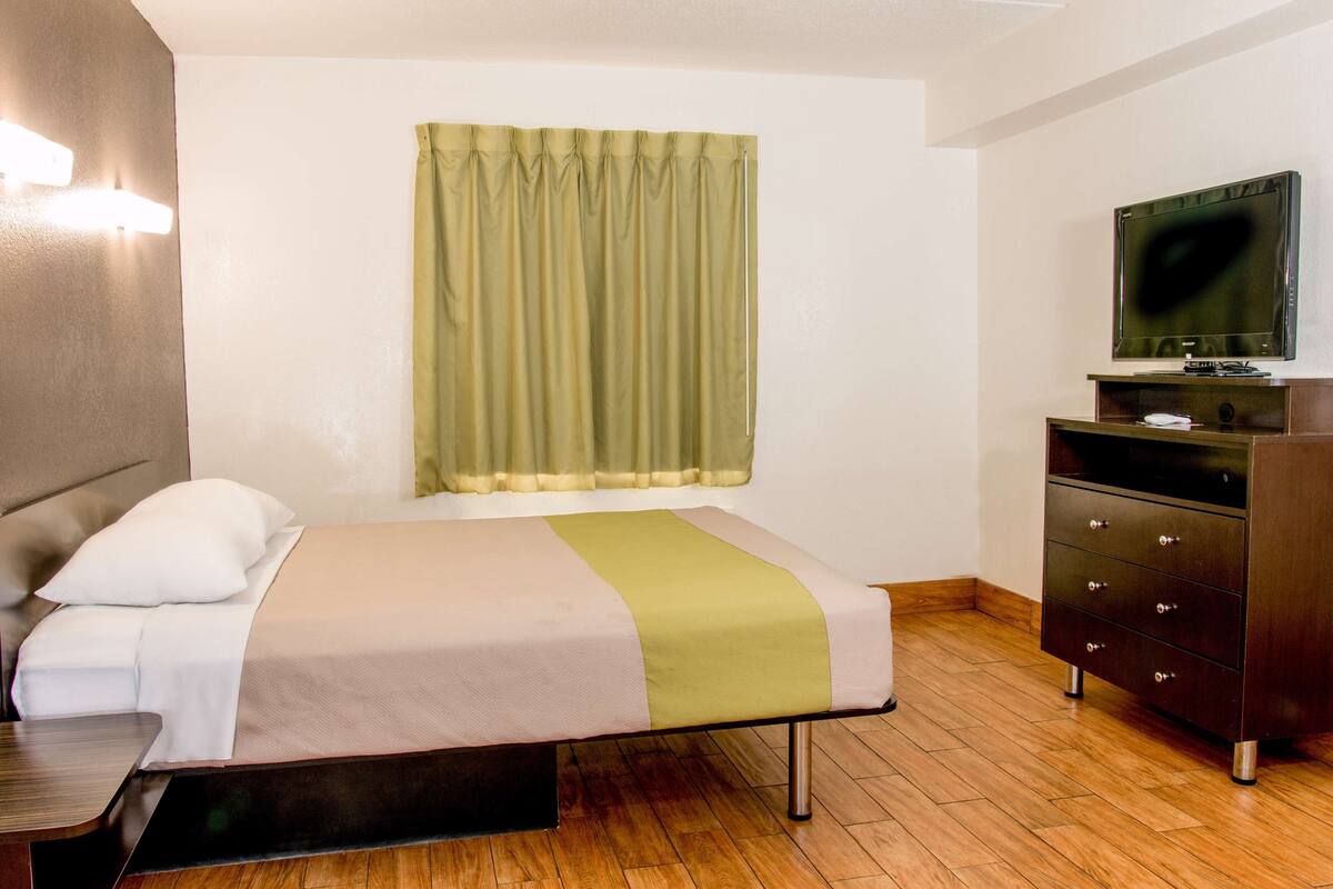 Une chambre d’hôtel avec un lit, une télévision, une commode et une fenêtre avec des rideaux.