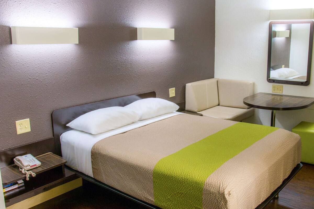 Une chambre d’hôtel avec un lit, une petite table, une chaise et un miroir au mur.