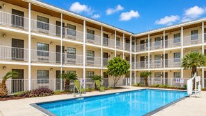 Un hôtel à plusieurs étages doté d’une piscine centrale, de balcons à chaque étage et offrant une vue sur un ciel d’un bleu éclatant.