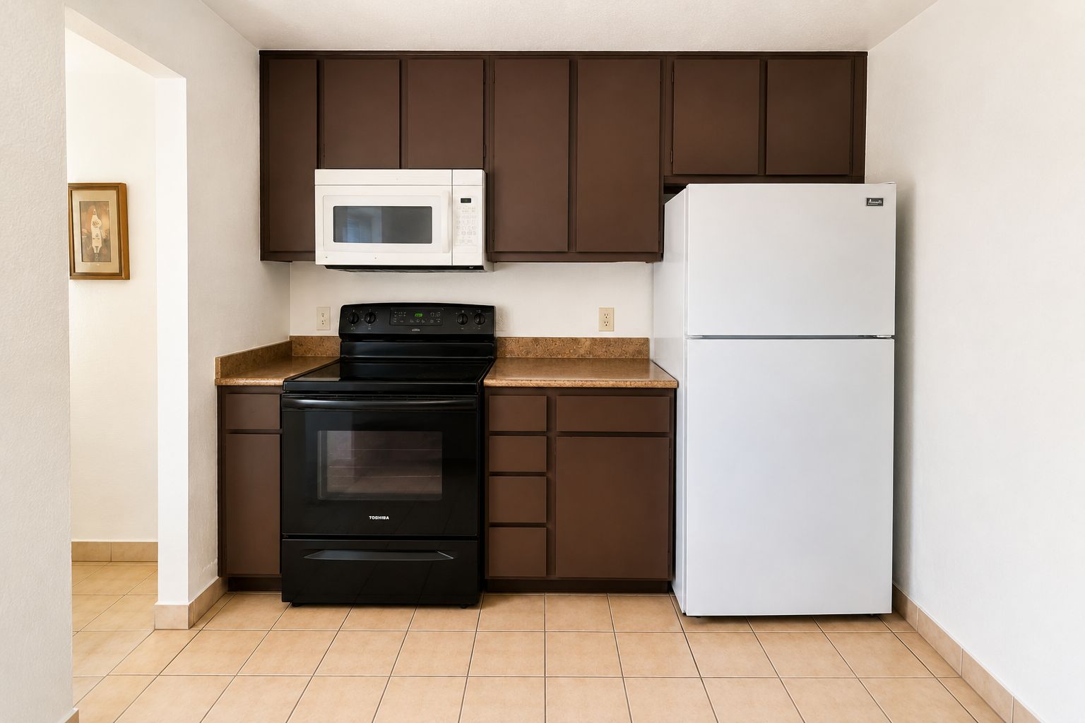 A compact kitchen with a black stove, a white microwave, and a white refrigerator.