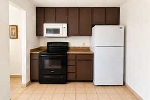 A compact kitchen with a black stove, a white microwave, and a white refrigerator. - Studio 6 San Antonio, TX - Lackland AFB (San Antonio)