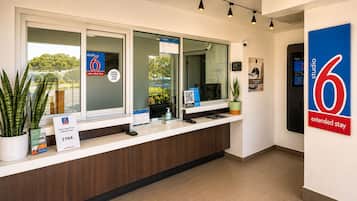 A hotel reception desk with a digital screen, a plant, and a sign indicating extended stay rates.