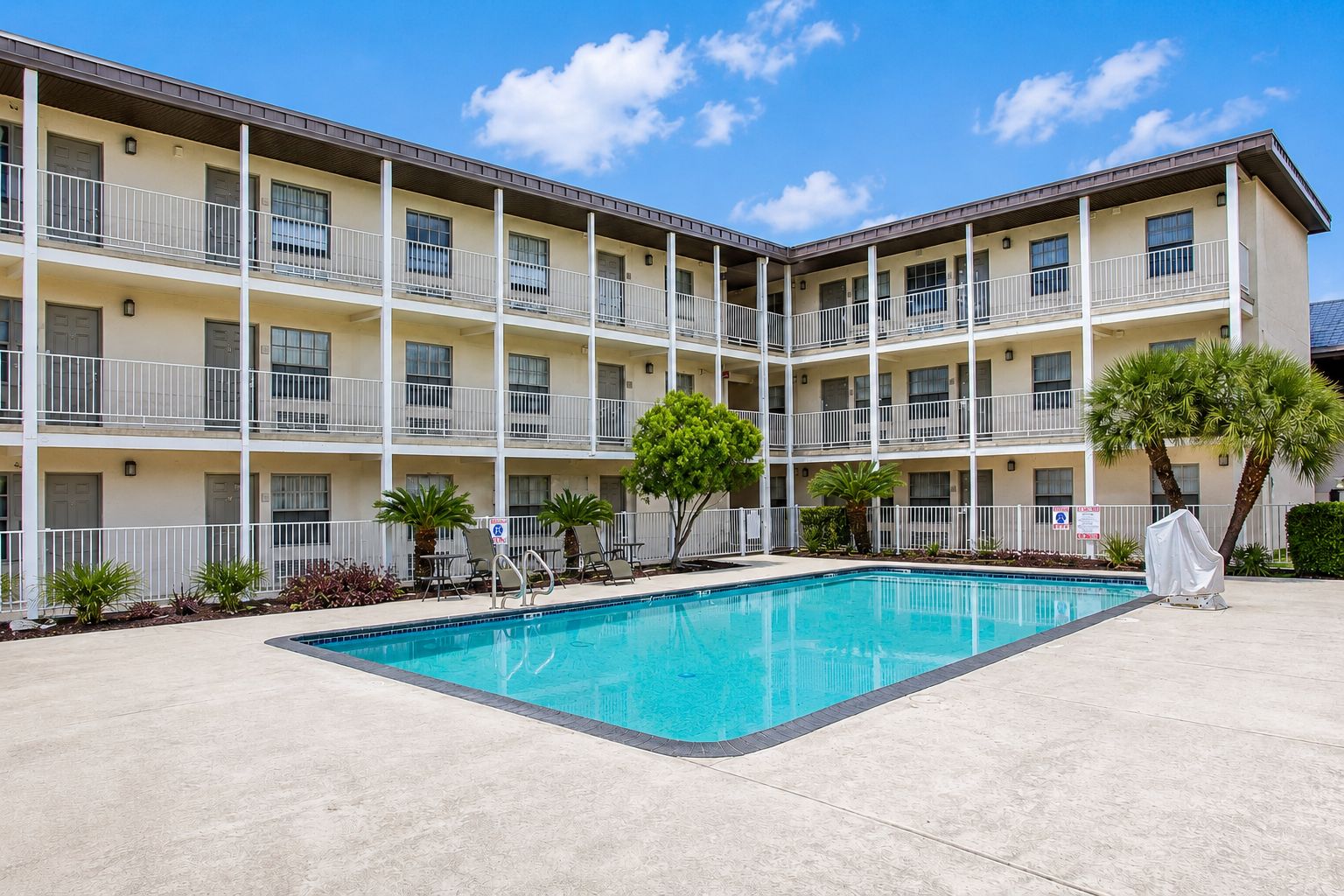 A multi-story hotel with a swimming pool, outdoor seating, and a covered area.