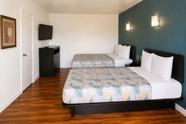 A hotel room with two beds, a television, a desk, and a wall-mounted light fixture.