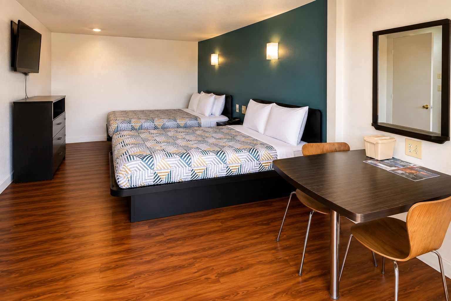A hotel room with a bed, a desk, a chair, a TV, and a mirror.