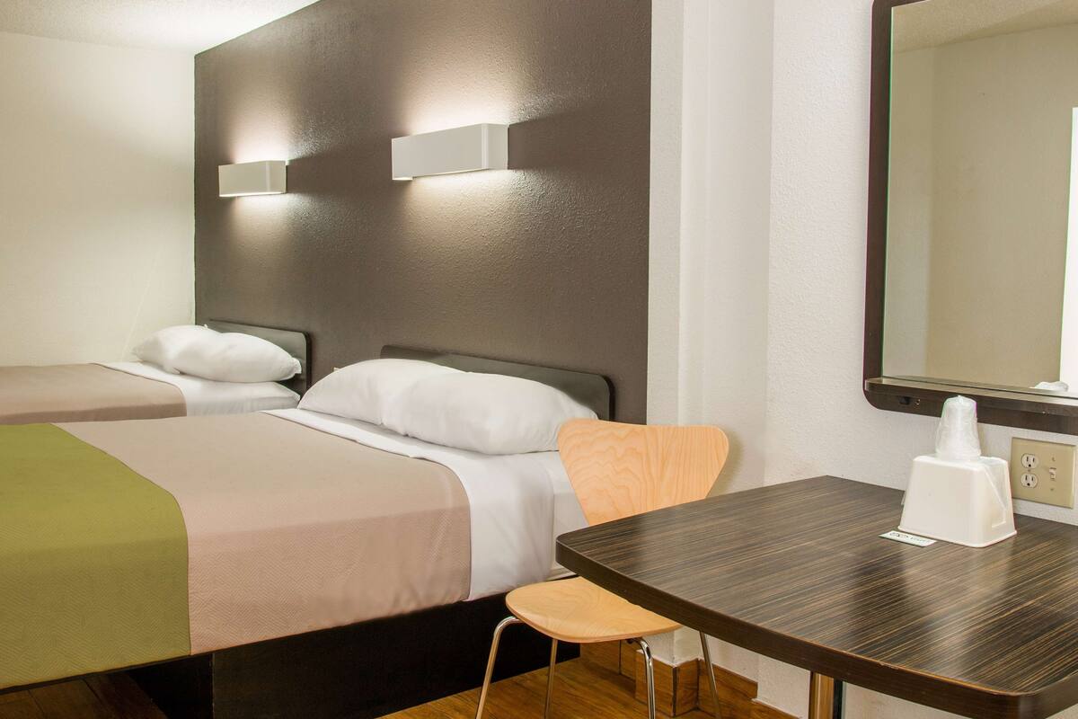 Une chambre d’hôtel avec deux lits, une chaise en bois, une table et un grand miroir.