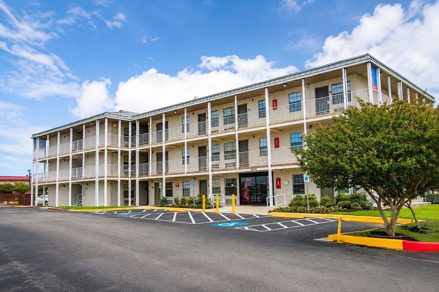 A multi-story hotel with a central entrance, a parking lot, and a tree in the foreground.