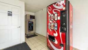 A vending machine with various beverage options, a water dispenser, and a restroom sign. - Motel 6 Troy, OH (Troy)