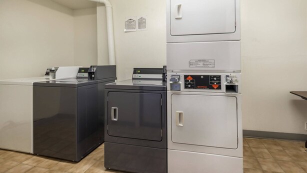 A laundry room with stacked washers and dryers, a water pipe, and a sign indicating the room's use. - Motel 6 Troy, OH (Troy)