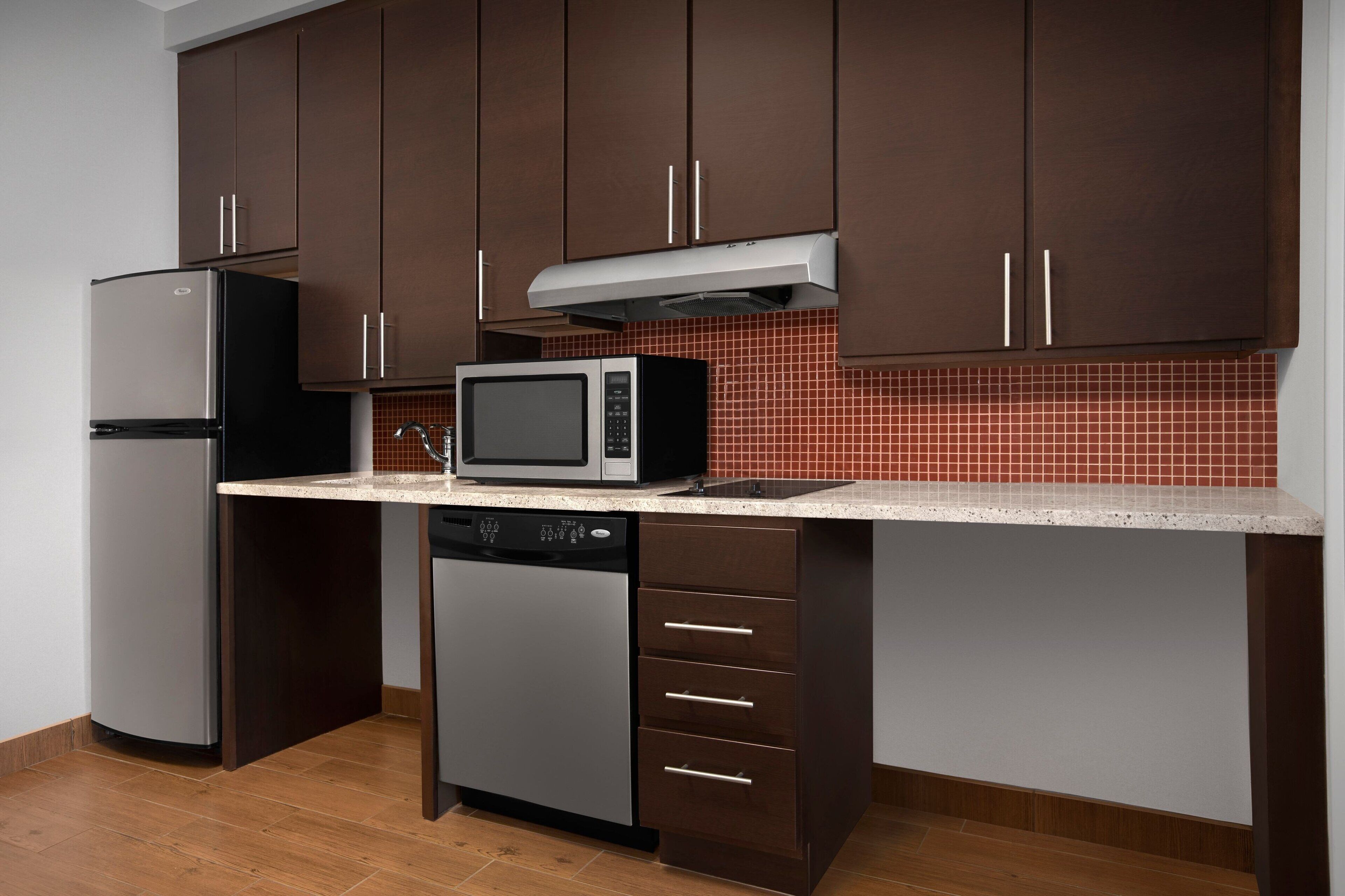 Una cocina con armarios de color marrón oscuro, un refrigerador de acero inoxidable, un microondas y un lavavajillas.