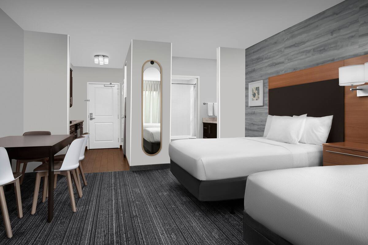 Une chambre d’hôtel avec un lit, un bureau avec des chaises, un miroir et une porte de salle de bain.