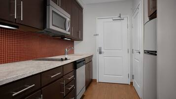 A modern kitchen with dark cabinets, a stainless steel microwave, a dishwasher, and a white door.