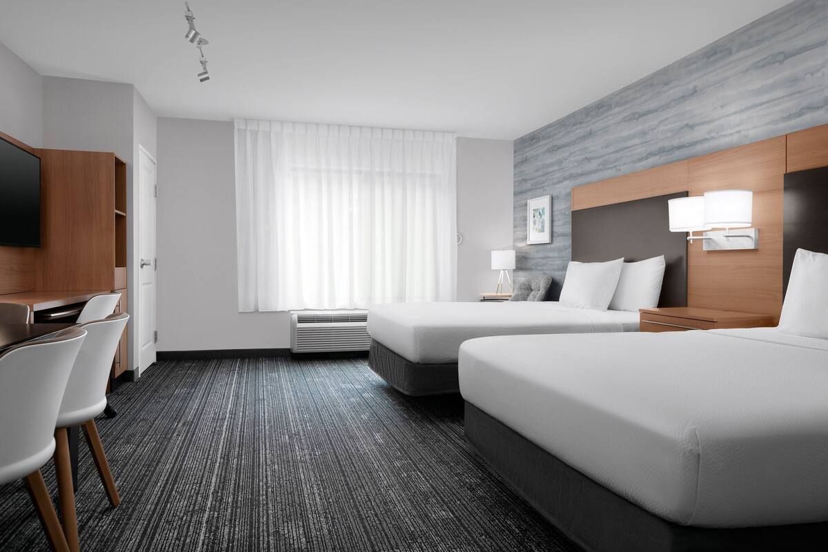 Une chambre d’hôtel avec deux lits, un bureau, une chaise, un téléviseur à écran plat et une fenêtre avec des rideaux.