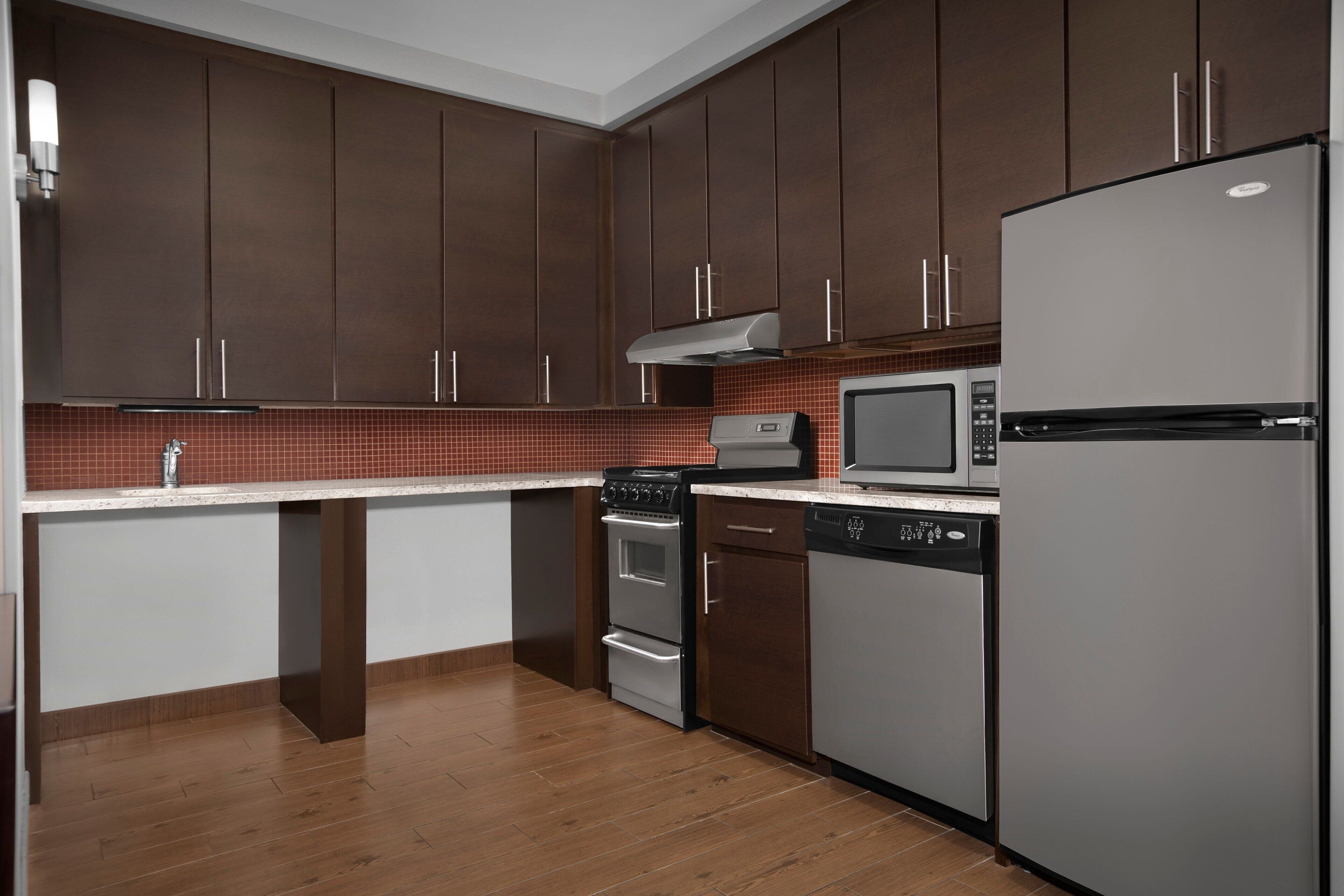 A modern kitchen with dark brown cabinets, a stainless steel refrigerator, a microwave, an oven, and a dishwasher.