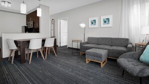 A modern hotel room with a dining area, grey sofa, and a small table. - TownePlace Suites Bridgeport Clarksburg (Clarksburg)