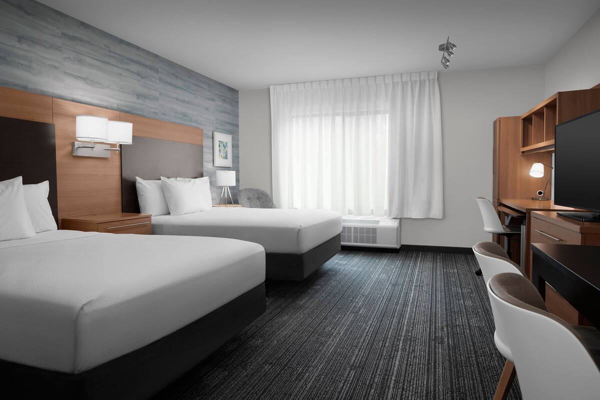 Une chambre d’hôtel avec deux lits, un bureau, une chaise, une télévision et une fenêtre avec des rideaux.