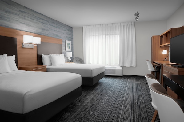 A hotel room with two beds, a desk, a chair, a TV, and a window with curtains.