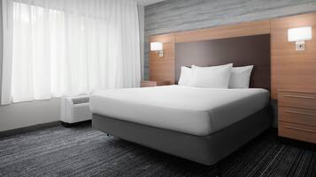 Una habitación de hotel moderna con una cama grande, dos mesitas de noche, una lámpara de pared y una ventana con cortinas translúcidas.