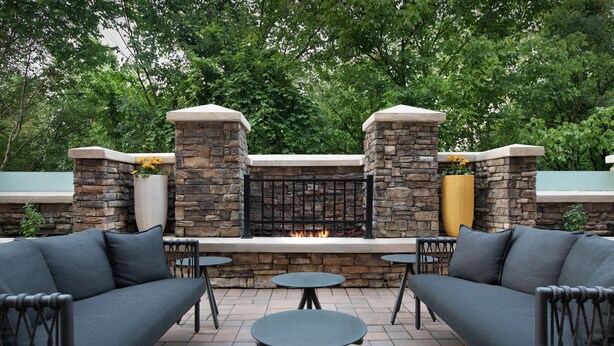 An outdoor patio area with stone walls, a built-in fire feature, and seating arrangements. - TownePlace Suites Bridgeport Clarksburg (Clarksburg)