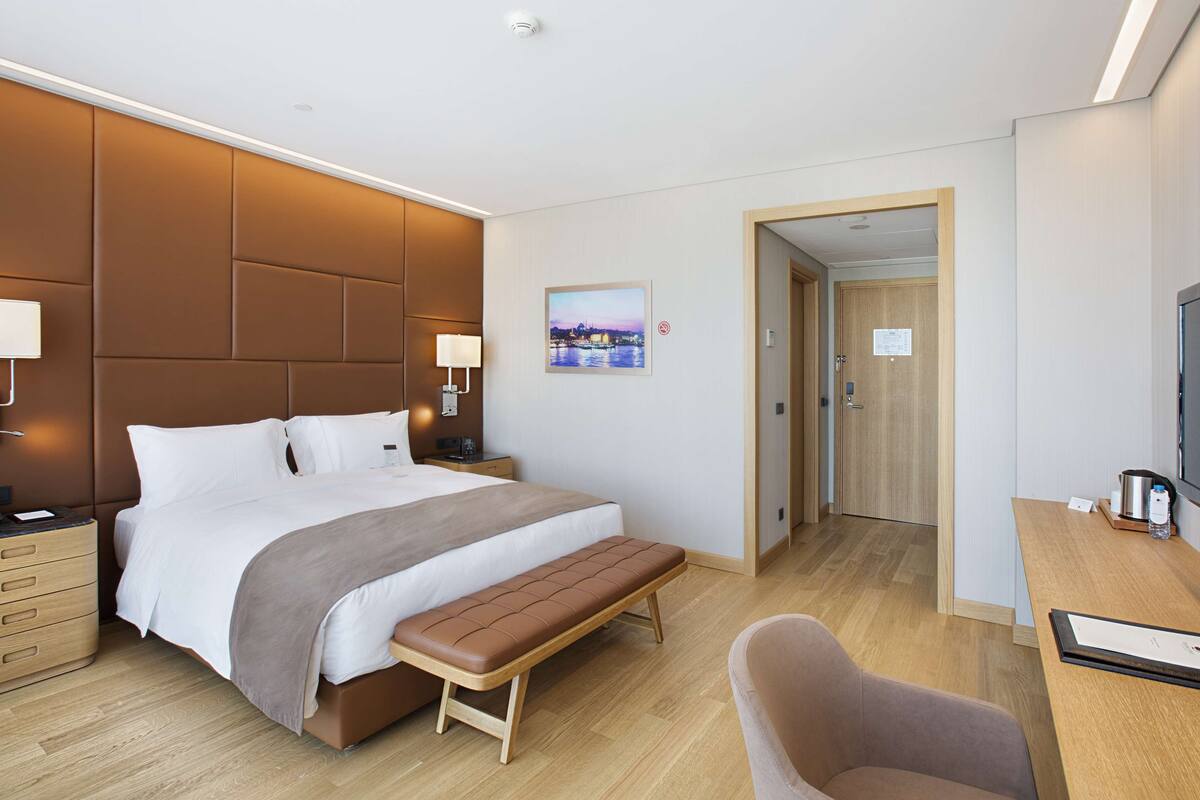 Una habitación de hotel moderna con una cama grande, mesitas de noche, un escritorio con una silla, un banco y un televisor.