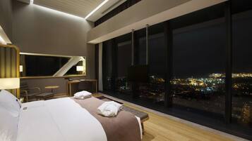 Una habitación de hotel moderna con una cama grande, un escritorio y vistas a un paisaje urbano nocturno.