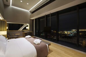 Una habitación de hotel moderna con una cama grande, un escritorio y vistas a un paisaje urbano nocturno.