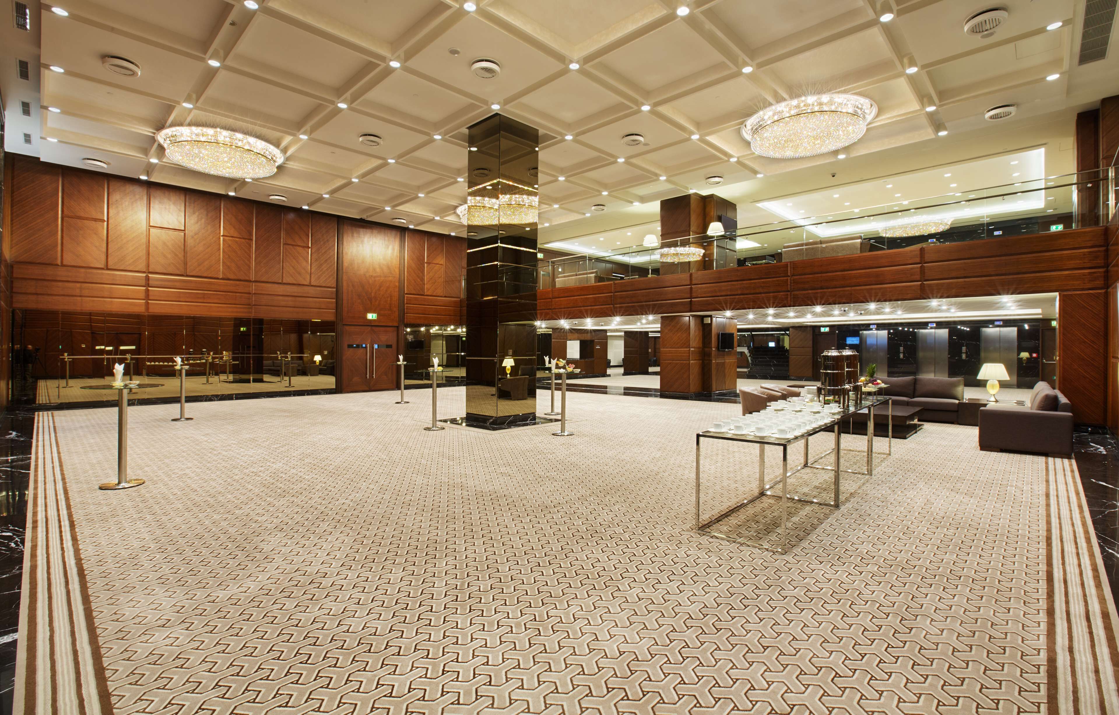 A spacious lobby with a high ceiling, chandeliers, a central column, and a seating area with a coffee table.