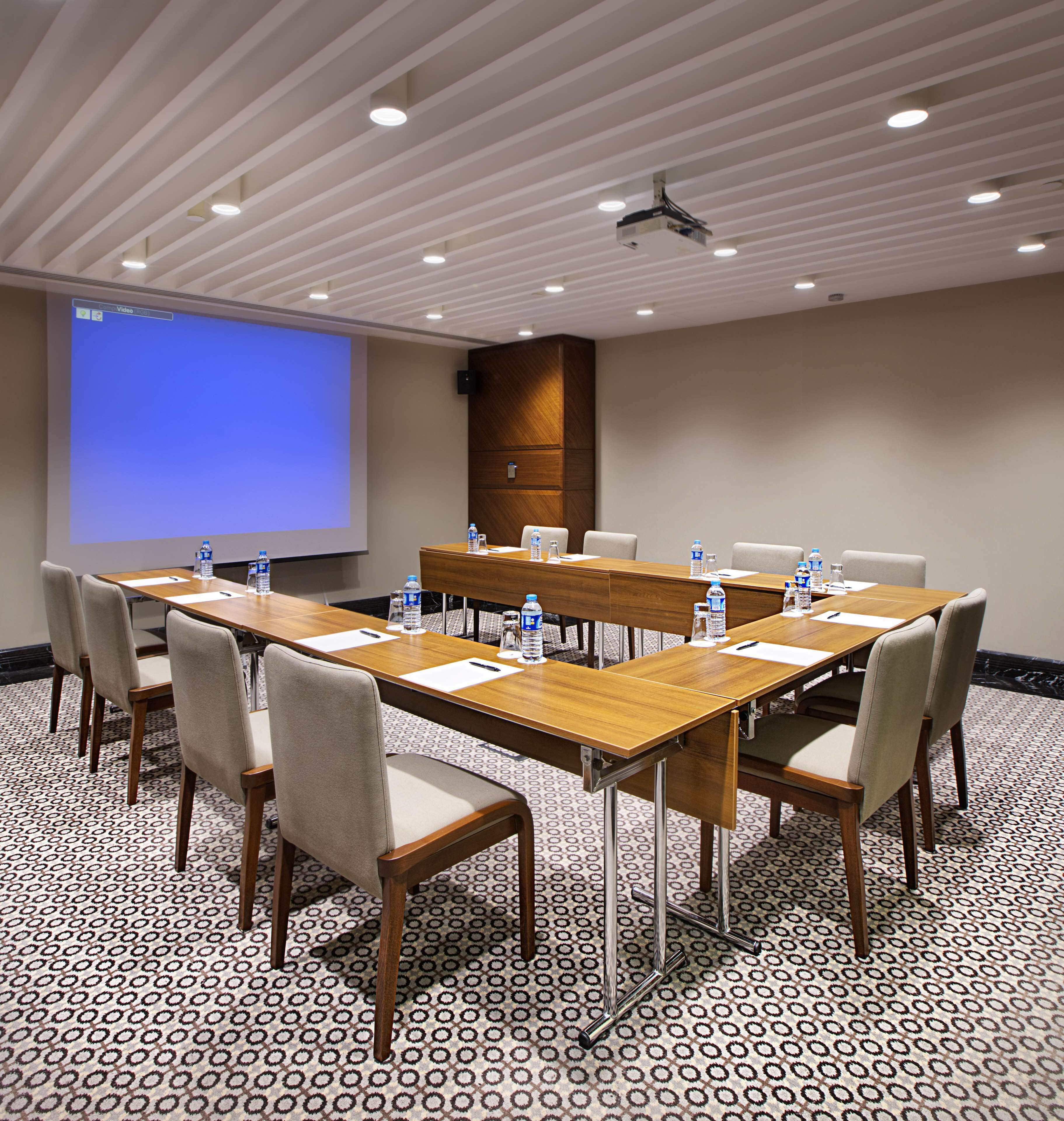 A conference room with a large table, chairs, a projector screen, and water bottles.