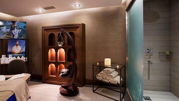 Un cuarto de spa con un mueble de madera, una silla de masaje, una mesita con toallas y una zona de ducha.
