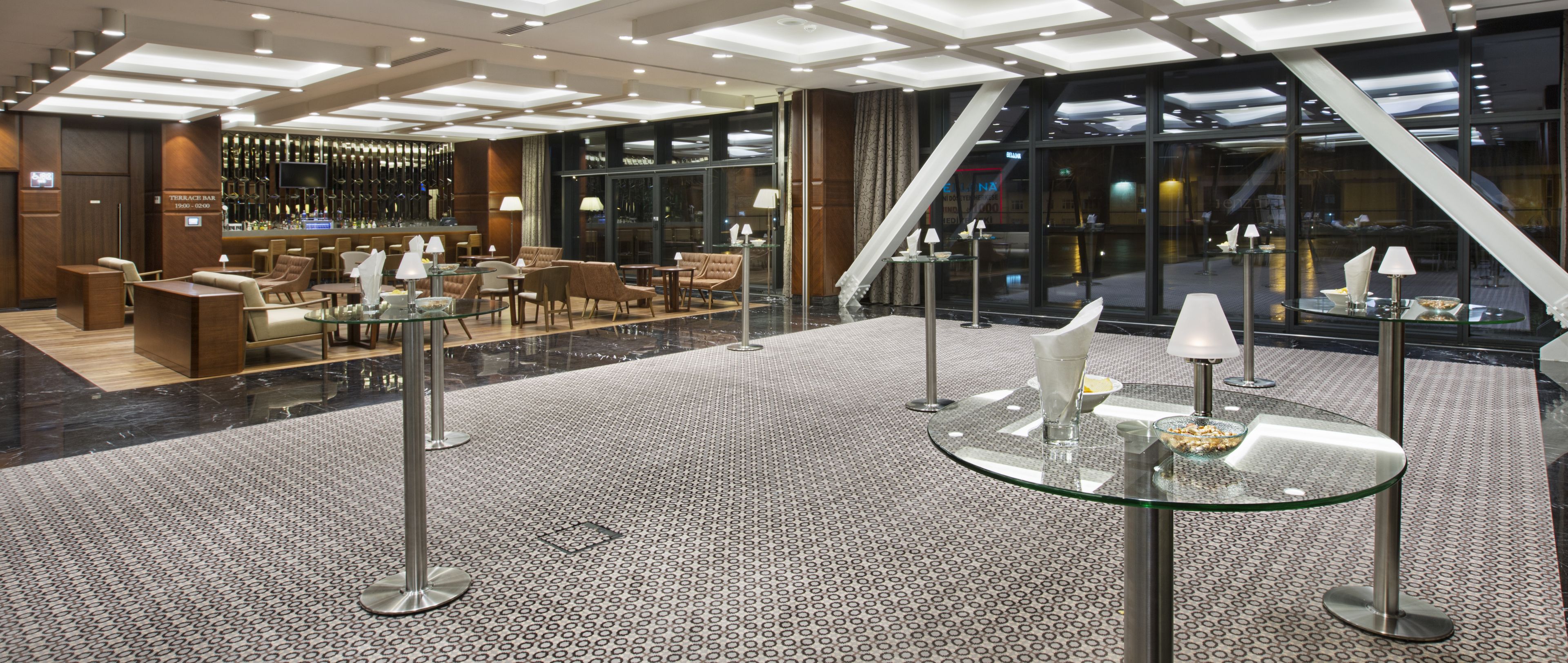 Un moderno hall de hotel con área de bar, disposición de asientos y una mesa de centro de vidrio.