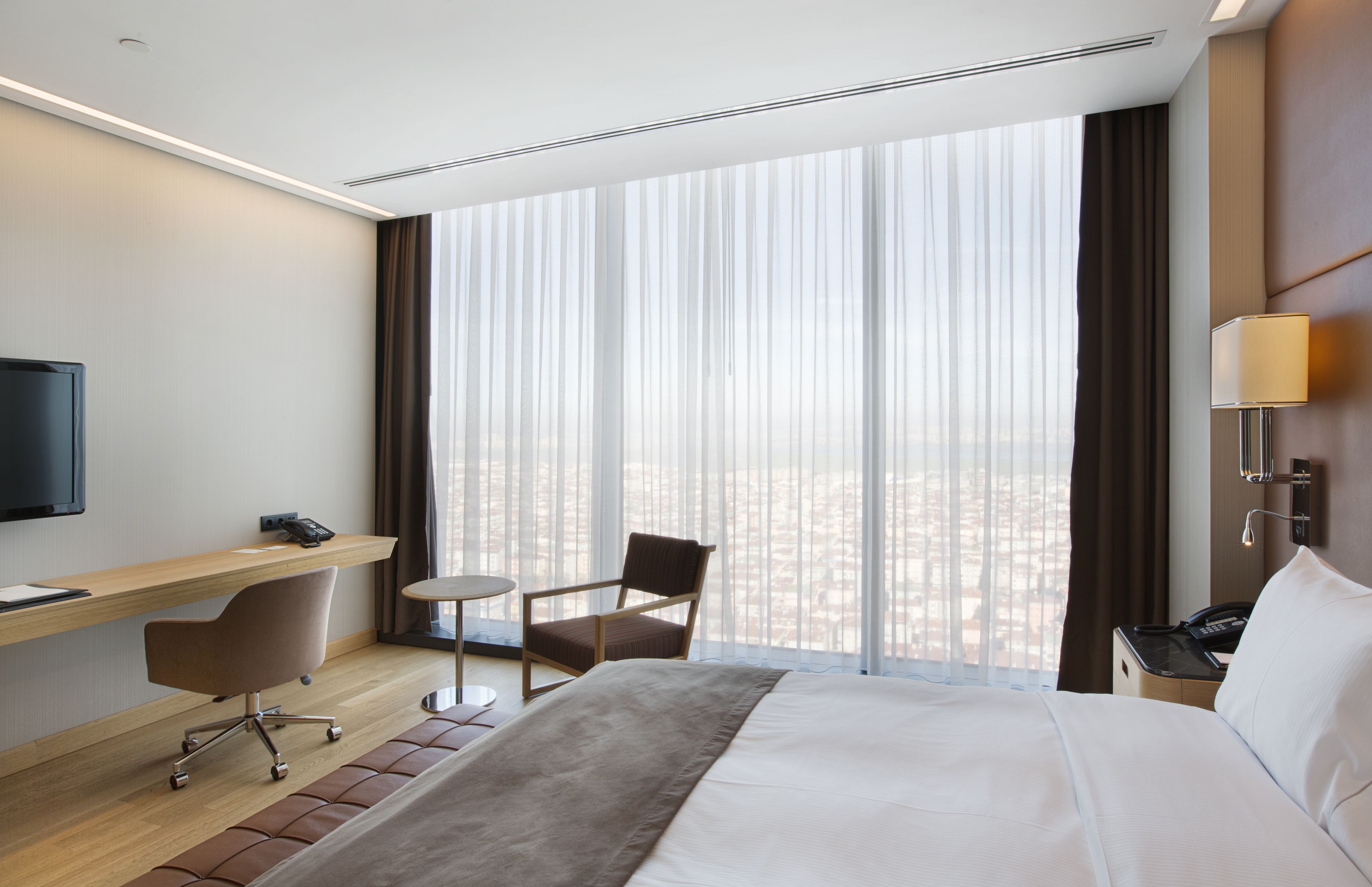A hotel room with a large bed, a desk, a chair, a TV, and a window with curtains.