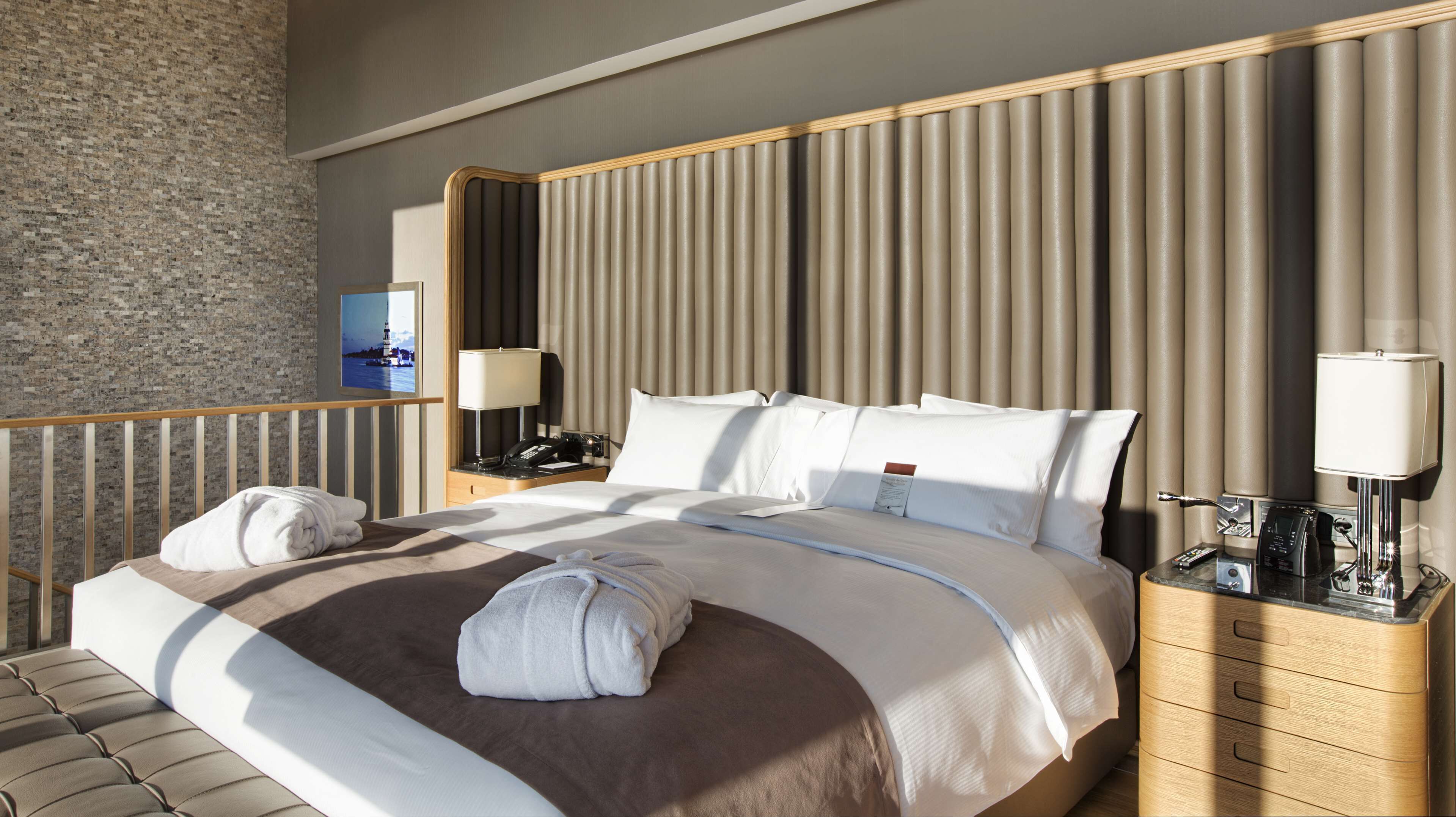 A hotel room with a large bed, two bedside tables, a nightstand, a lamp, a telephone, and a television on the wall.