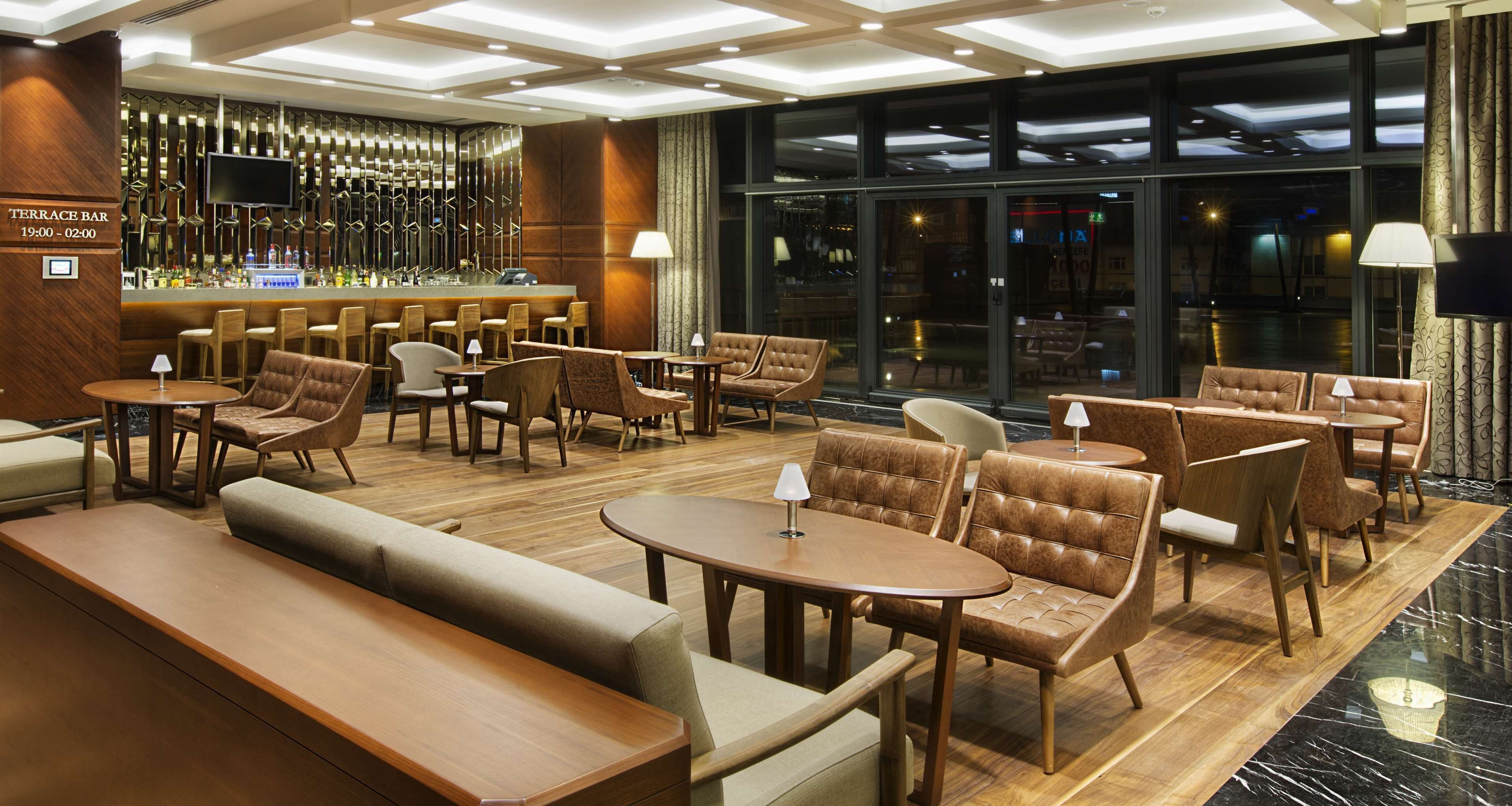 A modern bar area with seating, a bar counter, and a large window providing a view of the city at night.