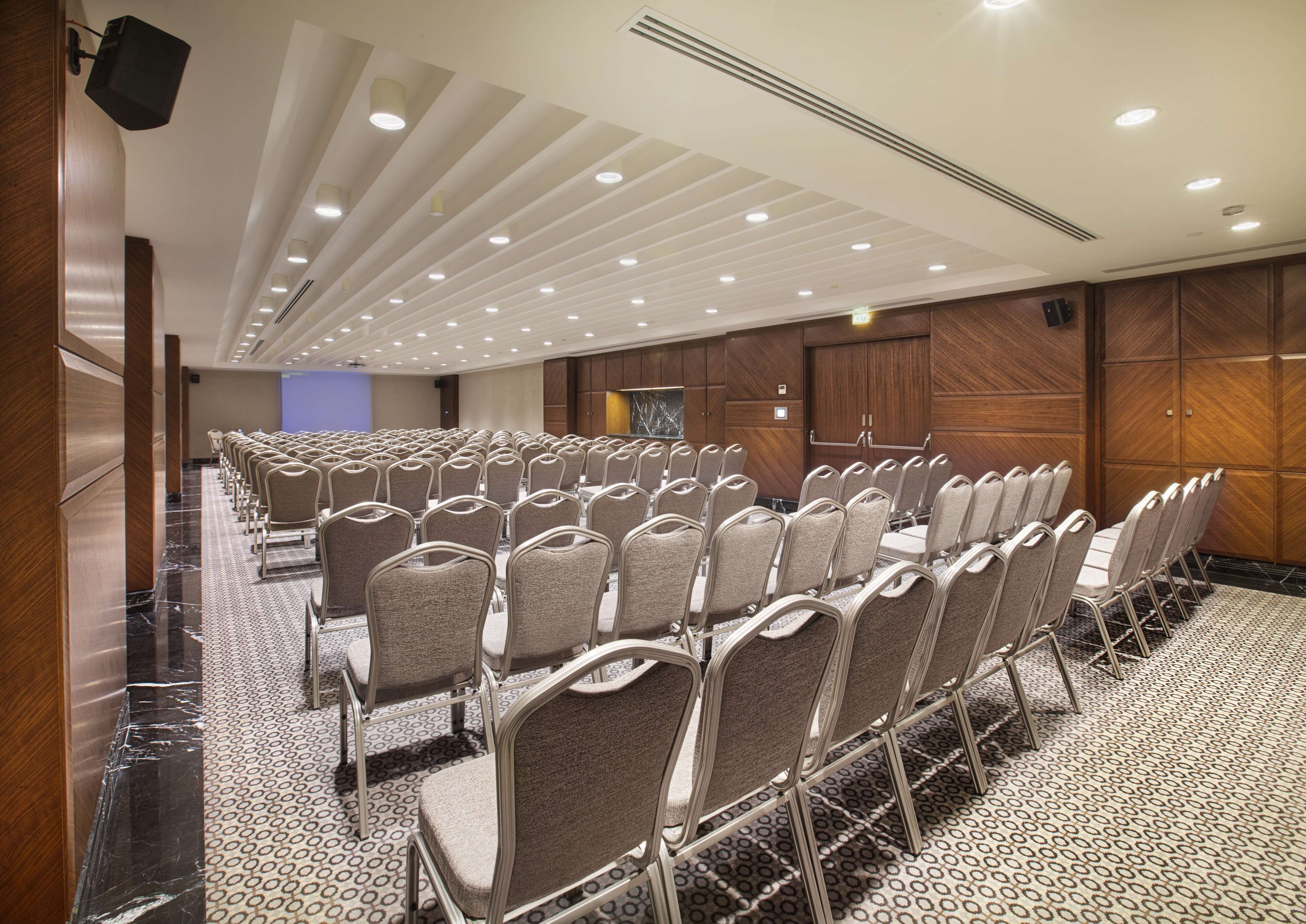 Un salón de conferencias con filas de sillas, piso de mármol y paneles de madera.