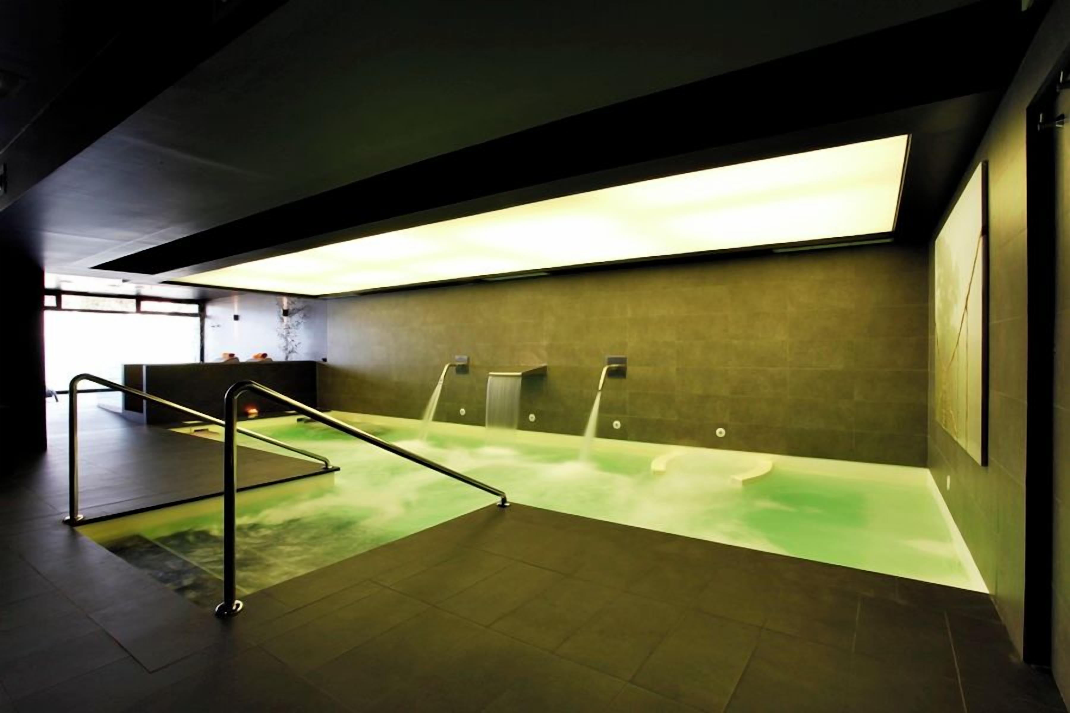 Une salle de bain moderne avec un sol éclairé de couleur verte, un banc et un lavabo fixé au mur.