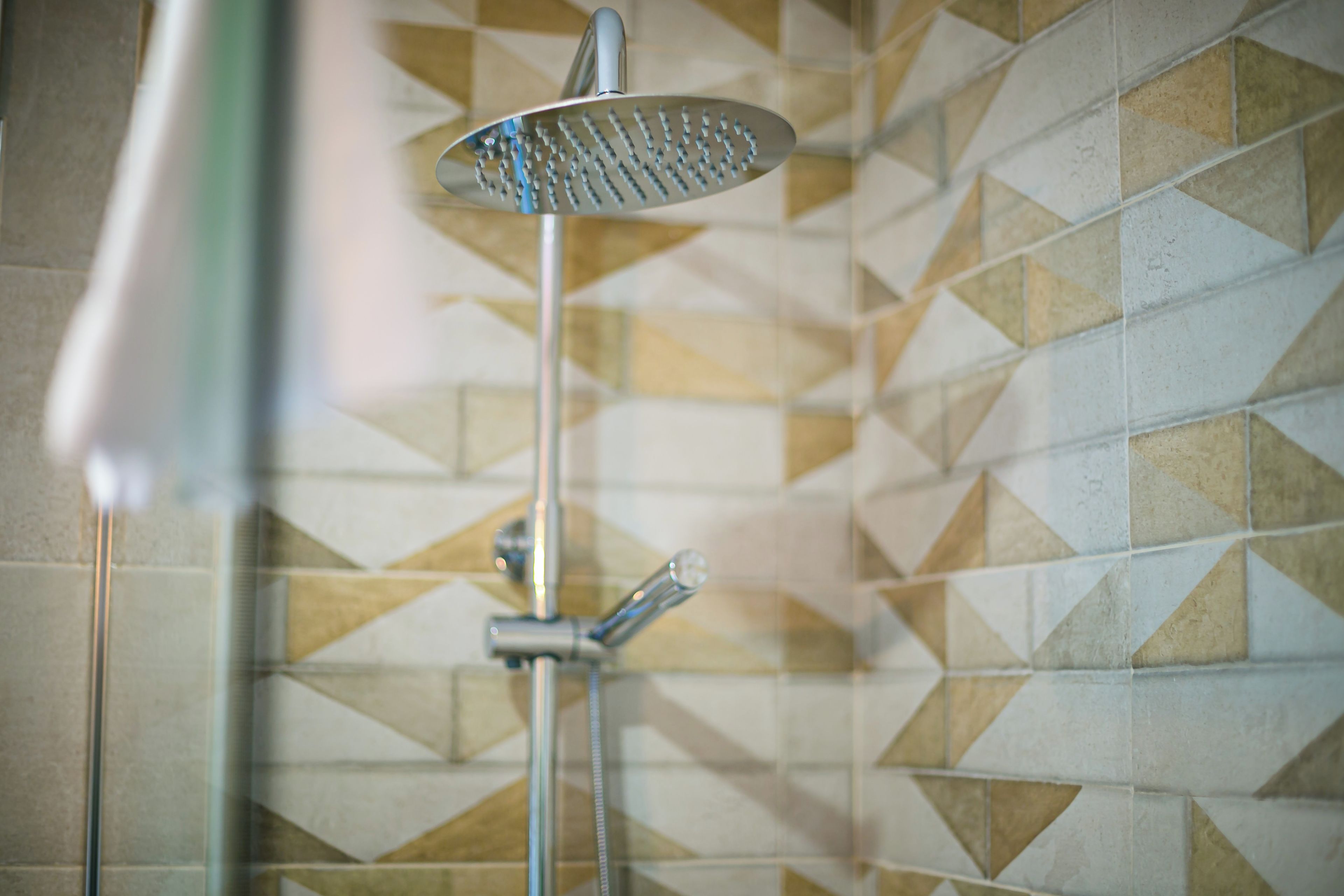 Ein Duschkopf mit Handbrause, an einer Wand mit geometrischem Fliesendesign angebracht.