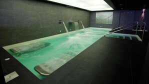 A spa area with a large hot tub, two wall-mounted water jets, and a staircase leading to an upper level. - La Sinagoga Hotel Spa (Hervas)