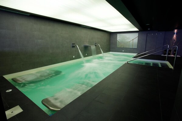 A spa area with a large hot tub, two wall-mounted water jets, and a staircase leading to an upper level. - La Sinagoga Hotel Spa (Hervas)