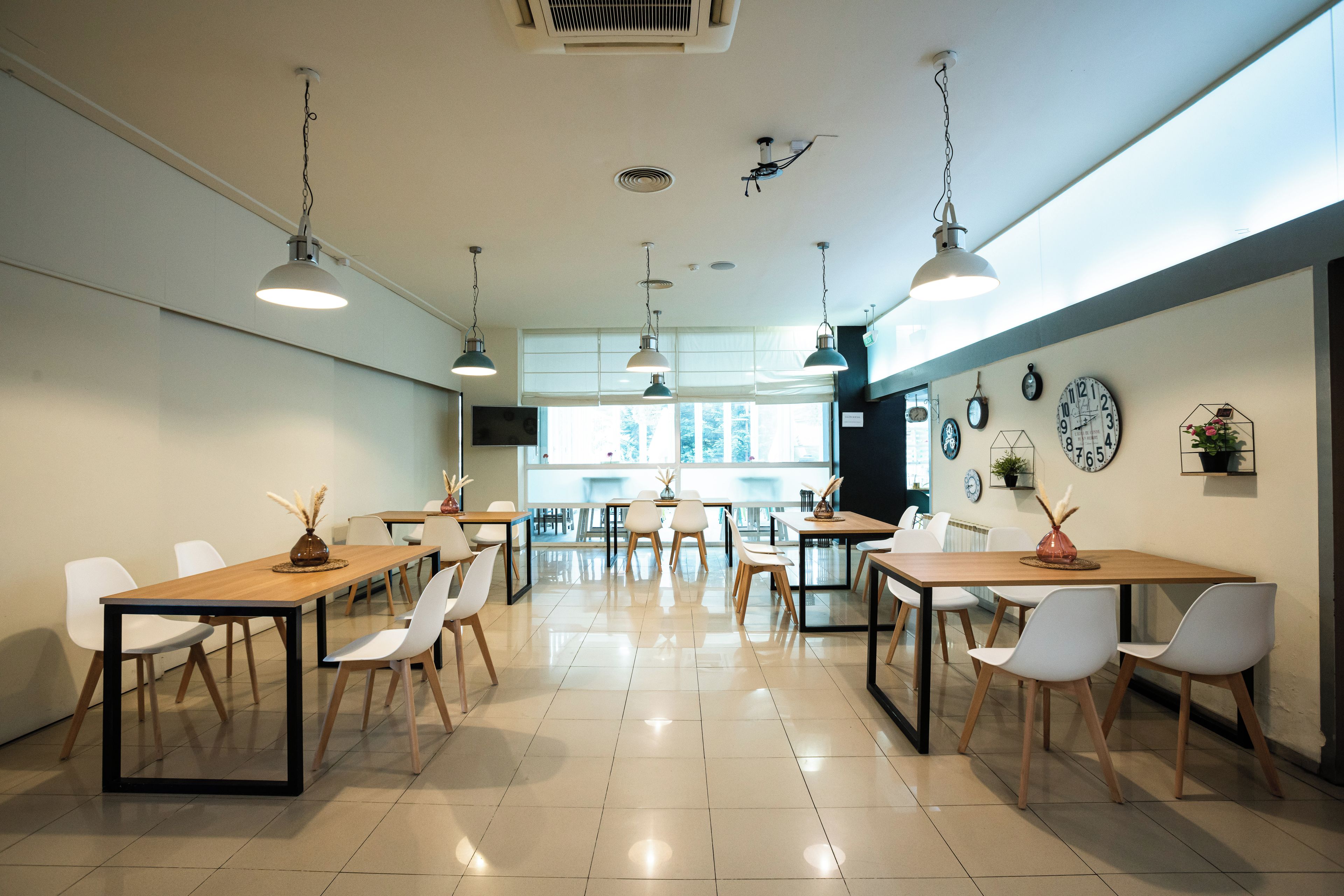 Un espace de restauration moderne, doté de tables et de chaises, d’un éclairage suspendu et d’horloges murales.