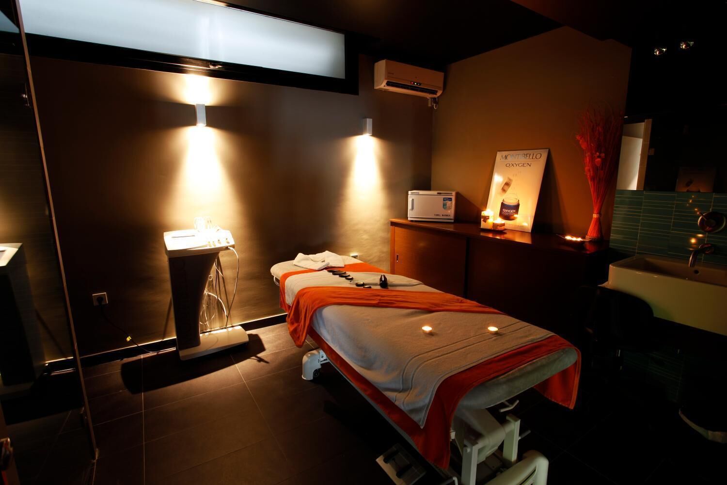 Une salle de spa moderne équipée d’une table de massage, d’un fauteuil de massage, d’un petit lavabo et d’un miroir.