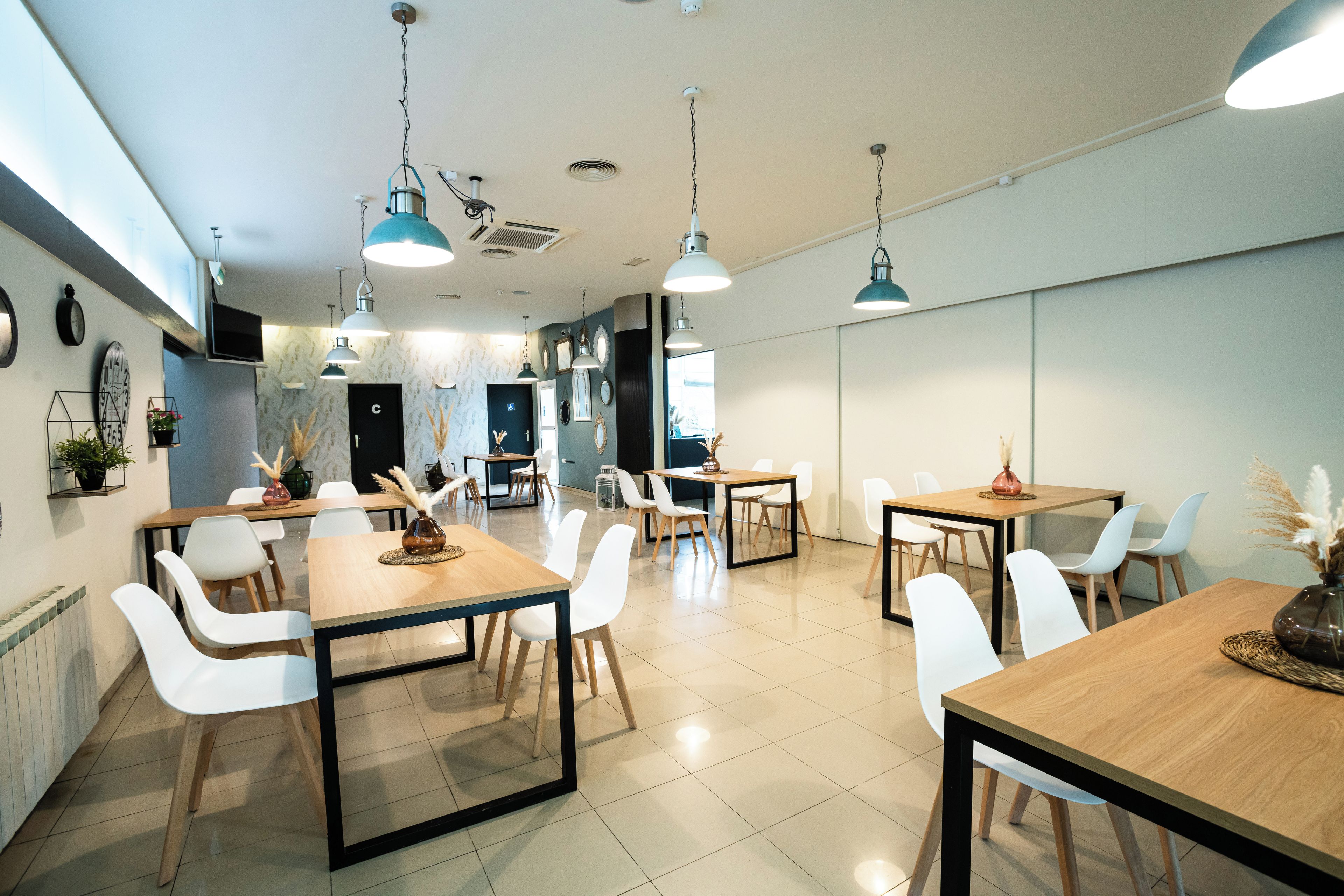 A modern dining area with multiple tables and chairs, pendant lighting, and a clean, minimalist design.