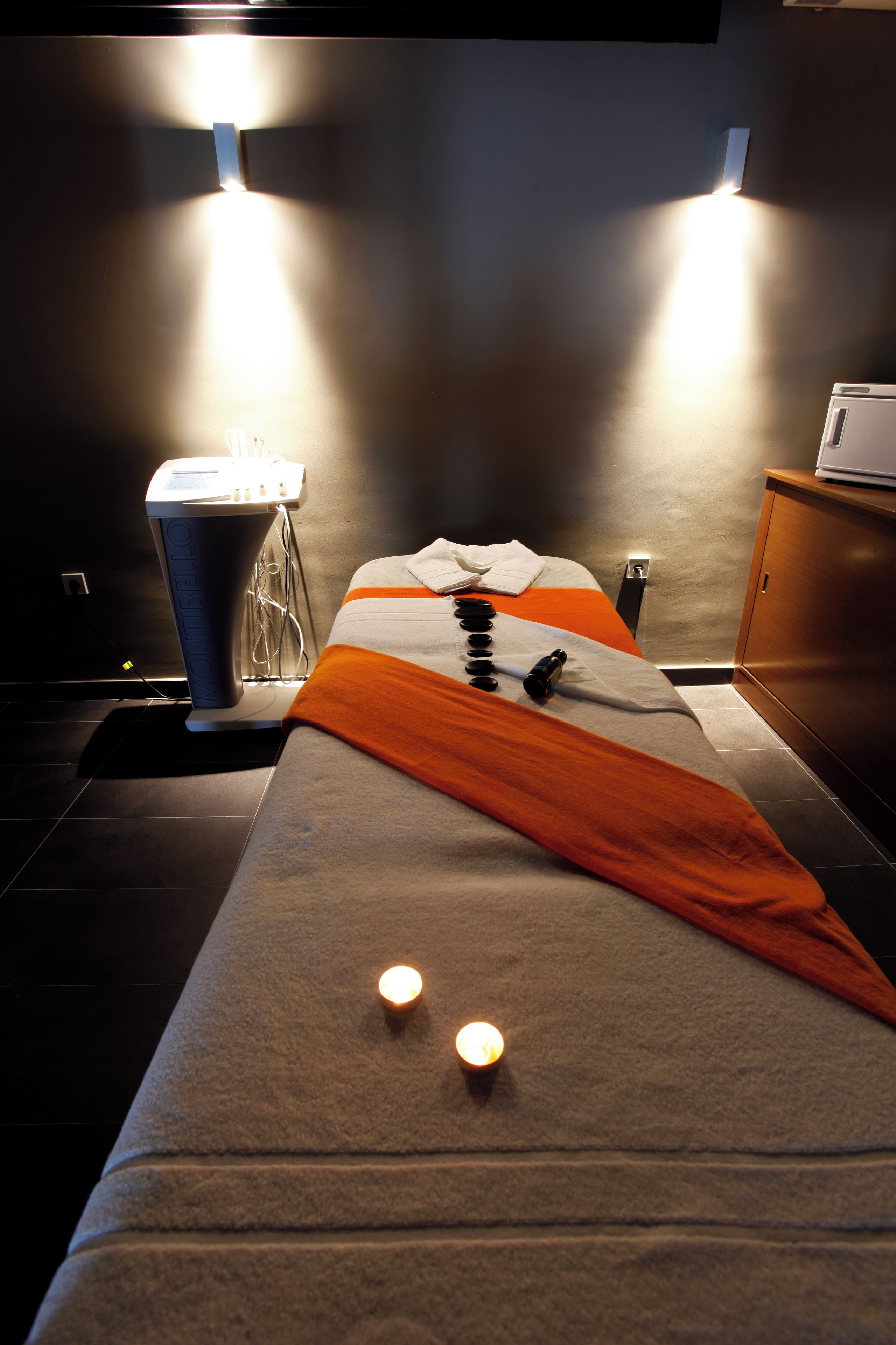 A massage table with a towel and a massage tool, a massage chair, and a cabinet.