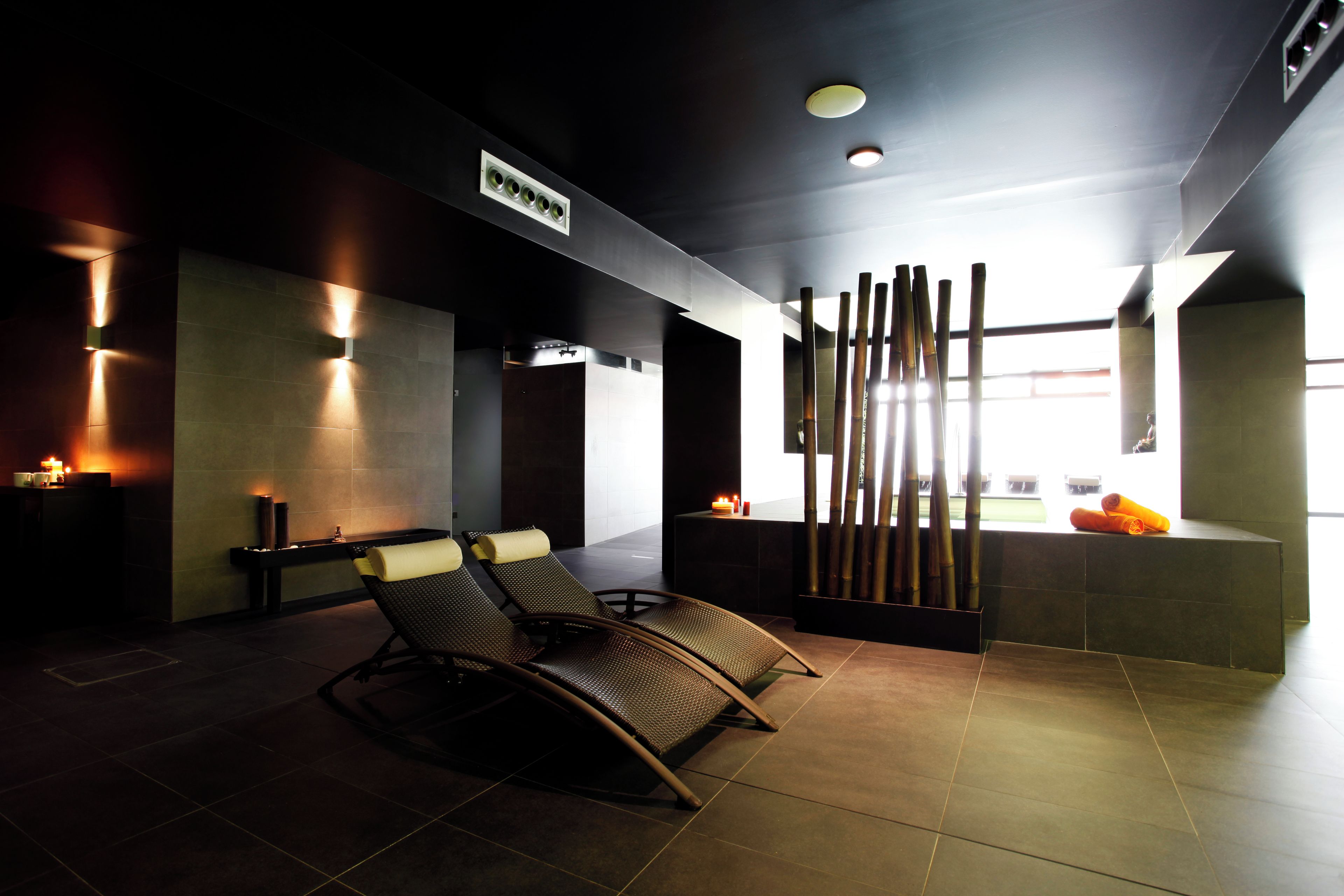 A modern spa room with a massage table, wall-mounted lights, and a view of the outdoors.
