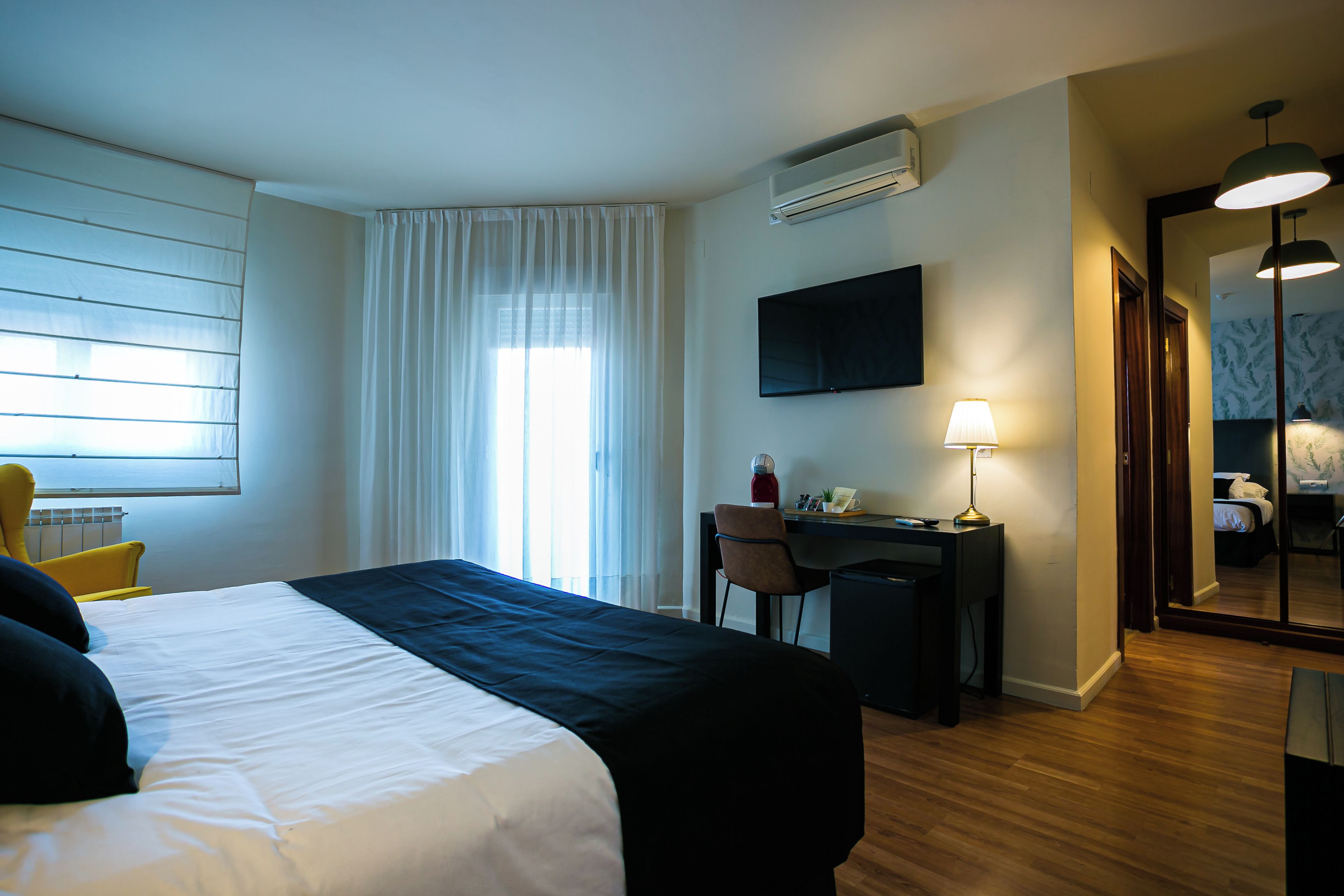 A hotel room with a bed, a desk, a chair, a TV, and a window with curtains.