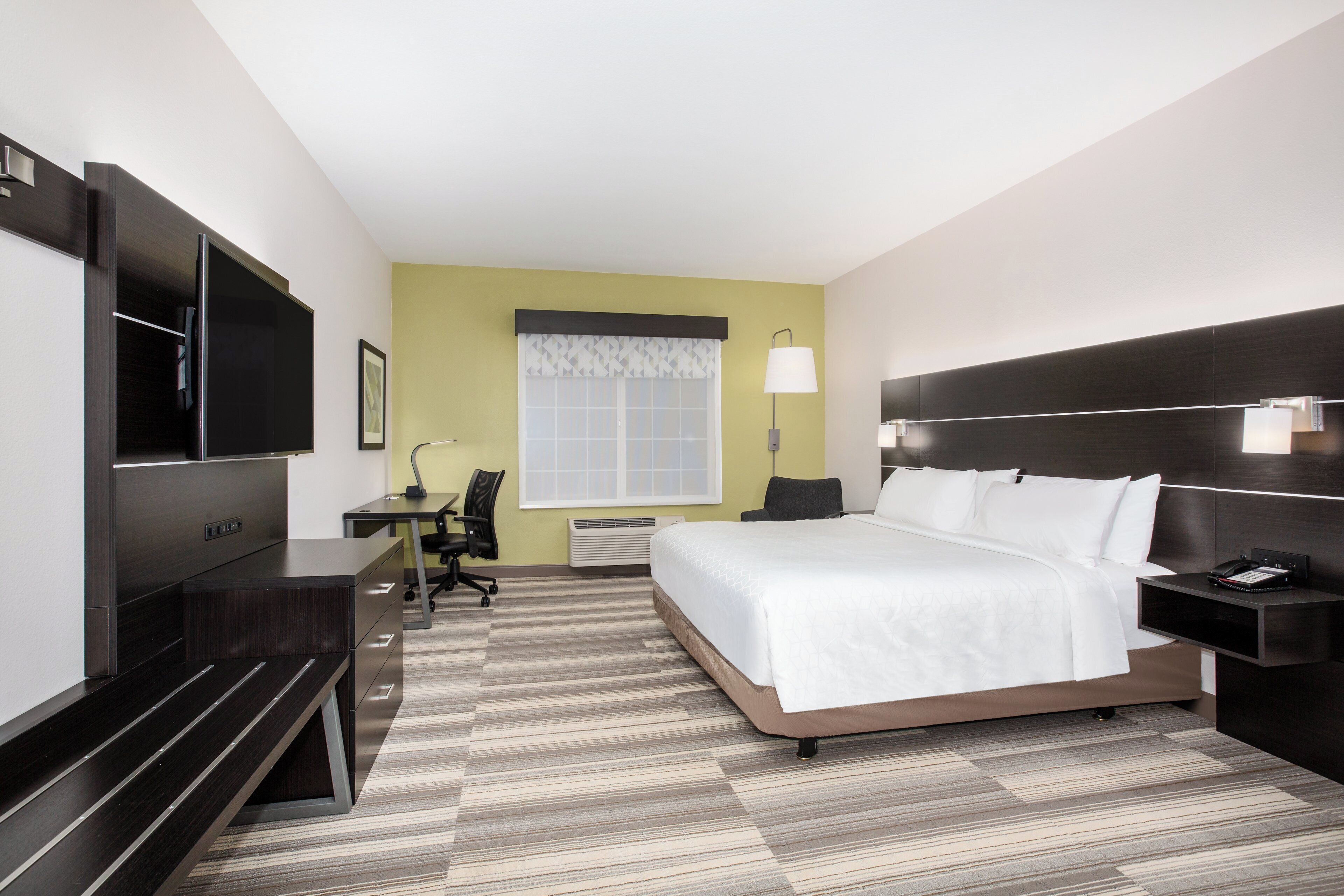 Een hotelkamer met een bed, bureau, stoel, televisie en een raam met gordijnen.