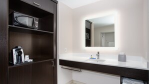 Un baño moderno con tocador de madera oscura, microondas, cafetera y espejo grande con iluminación integrada.